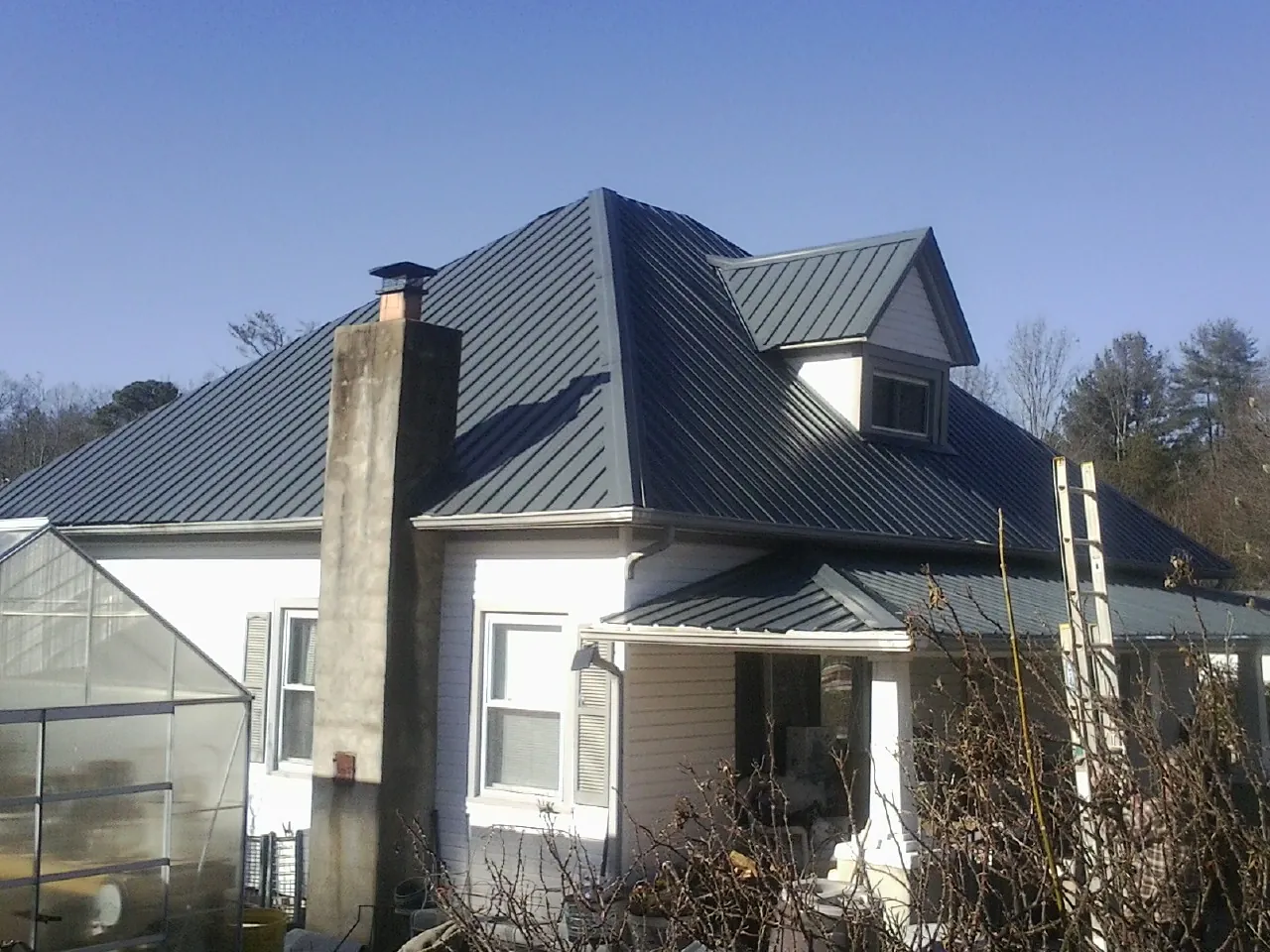 Dark blue standing seam metal roof on a white farmhouse with dormer — Slate & Tile Roof Repair by Roofing Brothers in Monticello
