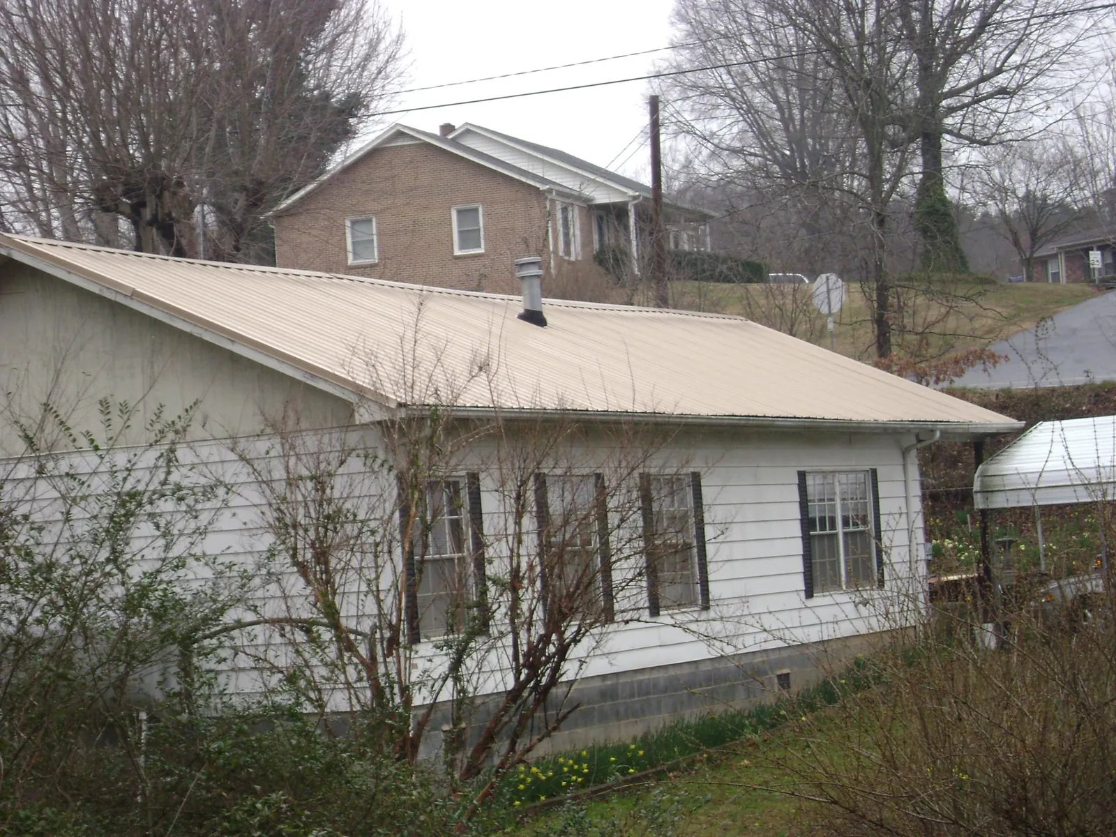 Tan metal roof on a white sided house set into a hillside — Commercial Roofing by Roofing Brothers in Monticello